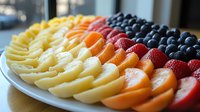 Fresh rainbow fruit platter with sliced pineapple, oranges, strawberries and blueberries arranged in colorful rows on white plate, healthy food styling.
