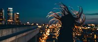 Young woman with flowing hair silhouetted against city skyline at dusk, urban lifestyle and freedom concept for modern living campaigns.