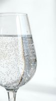 Clear glass filled with sparkling water showing carbonation bubbles against clean white background for beverage and refreshment concepts.