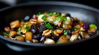 Roasted root vegetables with caramelized onions and dried fruits in dark ceramic bowl, garnished with fresh herbs. Seasonal autumn side dish.