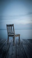 Weathered wooden chair sitting alone on a dock extending into calm water under moody blue sky, conveying solitude and contemplation for editorial and conceptual projects.
