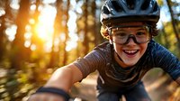 Young Asian woman cyclist in protective gear smiling while mountain biking through forest trail at sunset, dynamic action shot capturing joy and adventure.