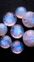 Luminous moonstone gemstones with iridescent blue and pink flashes arranged on dark surface for jewelry design and spiritual healing practices.