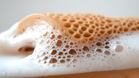 Macro shot of soap foam bubbles creating abstract honeycomb pattern in peach and white tones, showing delicate surface tension and organic shapes.