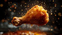 Crispy fried chicken leg with exploding breadcrumbs and spices against dark background with bokeh lights, dynamic food photography with motion effect.