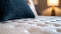 Close-up view of luxury mattress surface with quilted pattern and navy blue pillow, soft bedroom lighting creates cozy atmosphere for sleep and relaxation concepts.