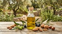 Extra virgin olive oil bottle with fresh olives, nuts and herbs on rustic wooden table in Mediterranean garden setting for culinary and cooking concepts.