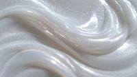 Smooth white cream with shimmering swirls and glossy texture creates luxurious cosmetic background for skincare product advertising.