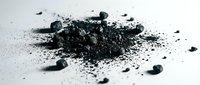 Pile of finely ground activated charcoal powder with scattered granules on white surface, suitable for skincare, detoxification, and wellness product marketing.
