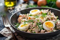 Fresh tuna salad with soft-boiled eggs, dill, and capers served in dark bowl, garnished with herbs and seasoning. Healthy protein-rich meal.