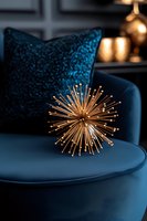 Modern gold starburst decorative sculpture on dark blue velvet sofa with sequin pillow creates luxurious home decor atmosphere in moody lighting.