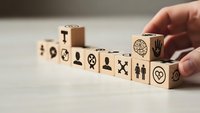 Hand arranging wooden blocks with business icons symbols for corporate strategy planning and team building concepts on desk surface.