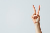 Hand showing peace sign or victory gesture against minimal light gray background, symbolizing positivity and success in communication.