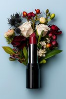 Red lipstick with blooming flowers arrangement featuring roses, thistles, and small buds on light blue background, creative cosmetic flatlay composition.