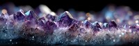 Panoramic view of amethyst crystal formation with purple peaks and translucent structures against dark background, showcasing natural mineral growth.