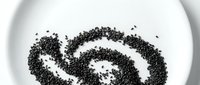 Poppy seeds arranged in spiral pattern on white plate, overhead view for food styling and culinary design projects.