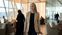 Professional blonde businesswoman in beige blazer standing confidently in modern corporate office lobby with glass walls and contemporary furniture.