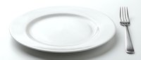 Empty white ceramic dinner plate with silver fork on white background, isolated tableware for restaurant menu, food blog, or catering design.