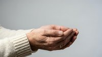 Elderly hands cupped together in protective gesture wearing cream knit sweater against neutral background for healthcare and care concepts.