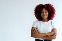 Confident young African American woman with curly red hair smiling with arms crossed wearing white t-shirt isolated on light background for design use.