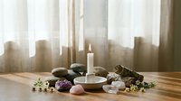 Spa wellness meditation setup with burning candle, healing crystals, stones and dried herbs on wooden table for relaxation and mindfulness practices.