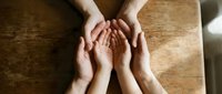 Four hands joined together in unity and support gesture on wooden table surface representing teamwork, collaboration and partnership concepts.