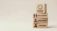Wooden blocks stacked with business icons showing customer service hierarchy from satisfaction to relationship management on neutral background.
