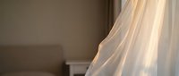 Sheer white curtain fabric billowing gently in soft natural light, creating an ethereal atmosphere suitable for home decor, interior design, and lifestyle content.
