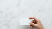 Hand holding blank white business card against marble surface for branding mockup and corporate identity presentation.