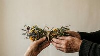 Elderly hands holding dried wildflower bouquet with twine against neutral background, suitable for wellness, nature, and lifestyle design projects.