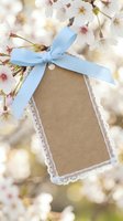 Blank kraft paper tag with blue ribbon hanging on blooming cherry blossom branch for spring greeting cards, gift labels, wedding invitations and craft projects.
