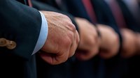 Close-up of businessman's hand in formal suit with blurred row of colleagues standing in line, representing corporate unity and professional teamwork.