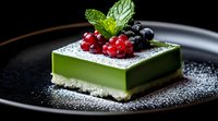 Modern matcha green tea dessert with fresh berries and mint garnish on black plate, dusted with powdered sugar. Elegant restaurant presentation.