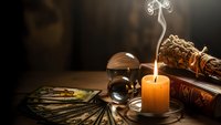 Mystical fortune telling setup with burning candle, tarot cards, crystal ball and ancient books creating atmospheric divination scene for spiritual guidance.