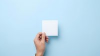 Hand holding blank pink sticky note against light blue background for messaging, branding, or advertising purposes.