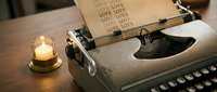 Vintage typewriter with paper typed with the word love repeatedly, glowing candle beside it on a wooden desk, romantic writing concept.