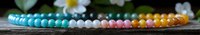 Colorful beaded bracelet with turquoise, white, pink and orange beads arranged in gradient pattern on rustic wooden surface with soft floral background.