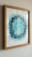 Framed watercolor artwork featuring hand-drawn marine life arranged in circular composition with seahorse, starfish, shells, and seaweed in turquoise and purple tones on white background. Perfect for coastal home decor.