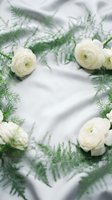 White ranunculus flowers with delicate green fern leaves arranged on soft fabric background for wedding invitations and romantic spring celebrations.