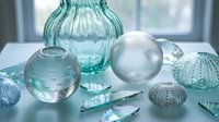 Transparent glass vases and spheres with sea urchin shells arranged on white surface near window, suitable for home decor and interior design styling.