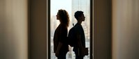 Two professional women in silhouette standing by office window discussing business strategy during corporate meeting in modern workplace.