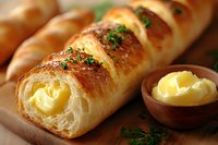Fresh baked bread roll filled with creamy butter and garnished with herbs on wooden board, close up view of flaky pastry texture and golden crust.