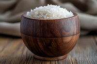 Steamed white jasmine rice served in wooden bowl on rustic table, close up view of traditional Asian cuisine with natural lighting and soft focus.