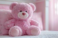 Pink plush teddy bear sitting on white bedding against soft pink background, creating gentle nursery atmosphere for children's room decor and baby photography.