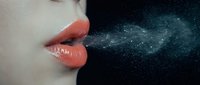 Woman with glossy coral lips exhaling sparkling stardust against dark cosmic background. Magical breath effect with glittering particles floating in space.
