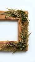 Wooden frame decorated with dried fern fronds and small white flowers arranged on white background for botanical and nature-themed design projects.