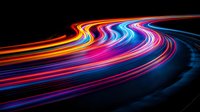 Vibrant light trails curve along dark road creating dynamic motion effect with neon colors of red, blue, orange and purple in long exposure night photography.