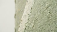 Cracked green paint peeling off white wall surface showing weathered deterioration and aging damage requiring maintenance and repair work.