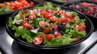 Fresh garden salad with crisp lettuce, juicy cherry tomatoes, red onions, and mixed greens served in black bowl, appetizing healthy food photography.