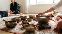 Sound healing therapy session with Tibetan singing bowls for meditation and wellness relaxation in bright modern room with natural light.